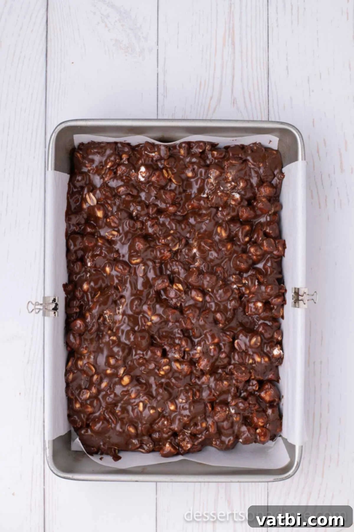 Decadent Rocky Road 6 The Rocky Road mixture, a blend of chocolate, peanuts, and marshmallows, evenly spread into a parchment-lined baking pan, ready for chilling.