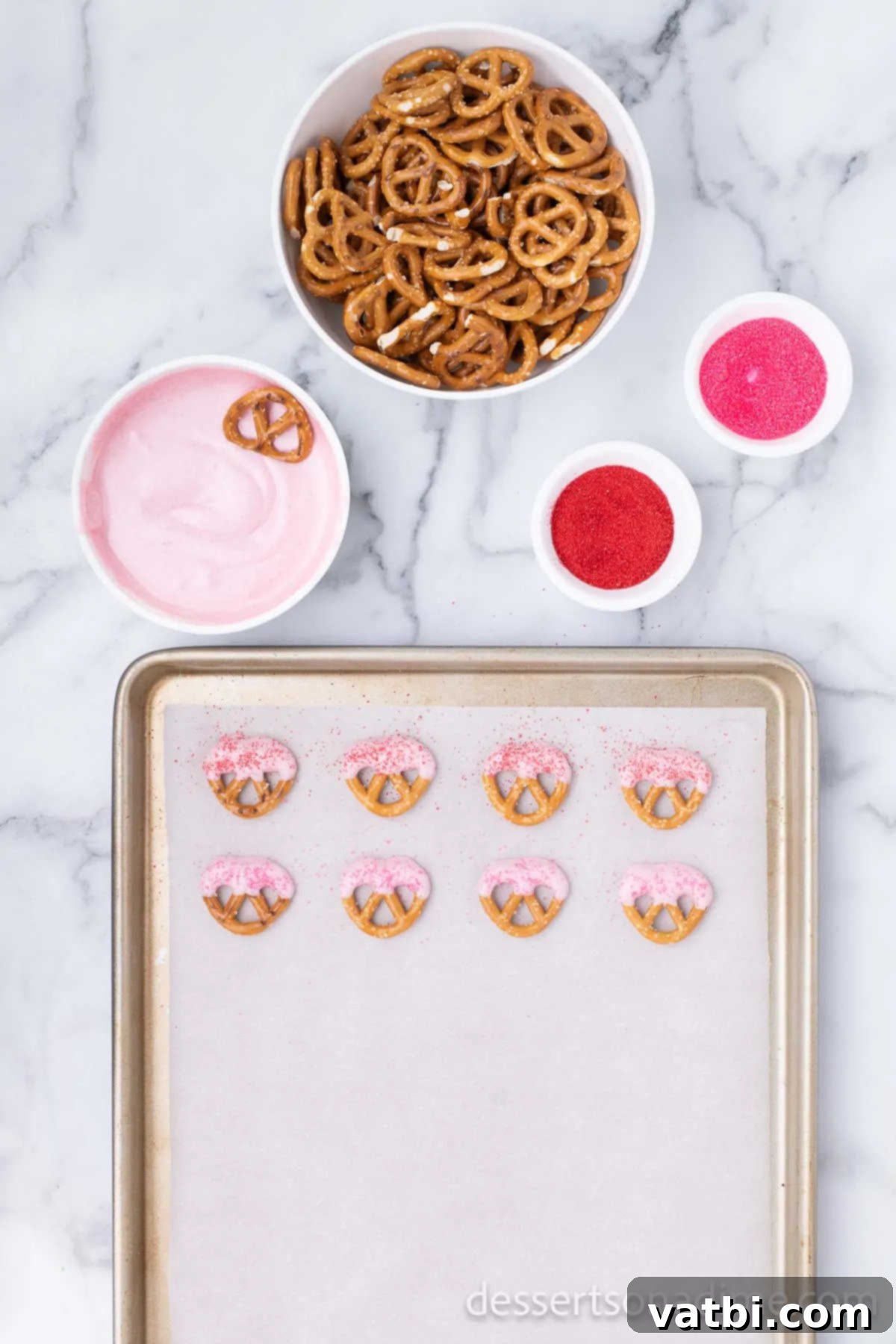 Love Crunch Pretzel Bites 2 Freshly dipped pretzels with pink and white chocolate, adorned with sprinkles and laid on parchment paper to dry.