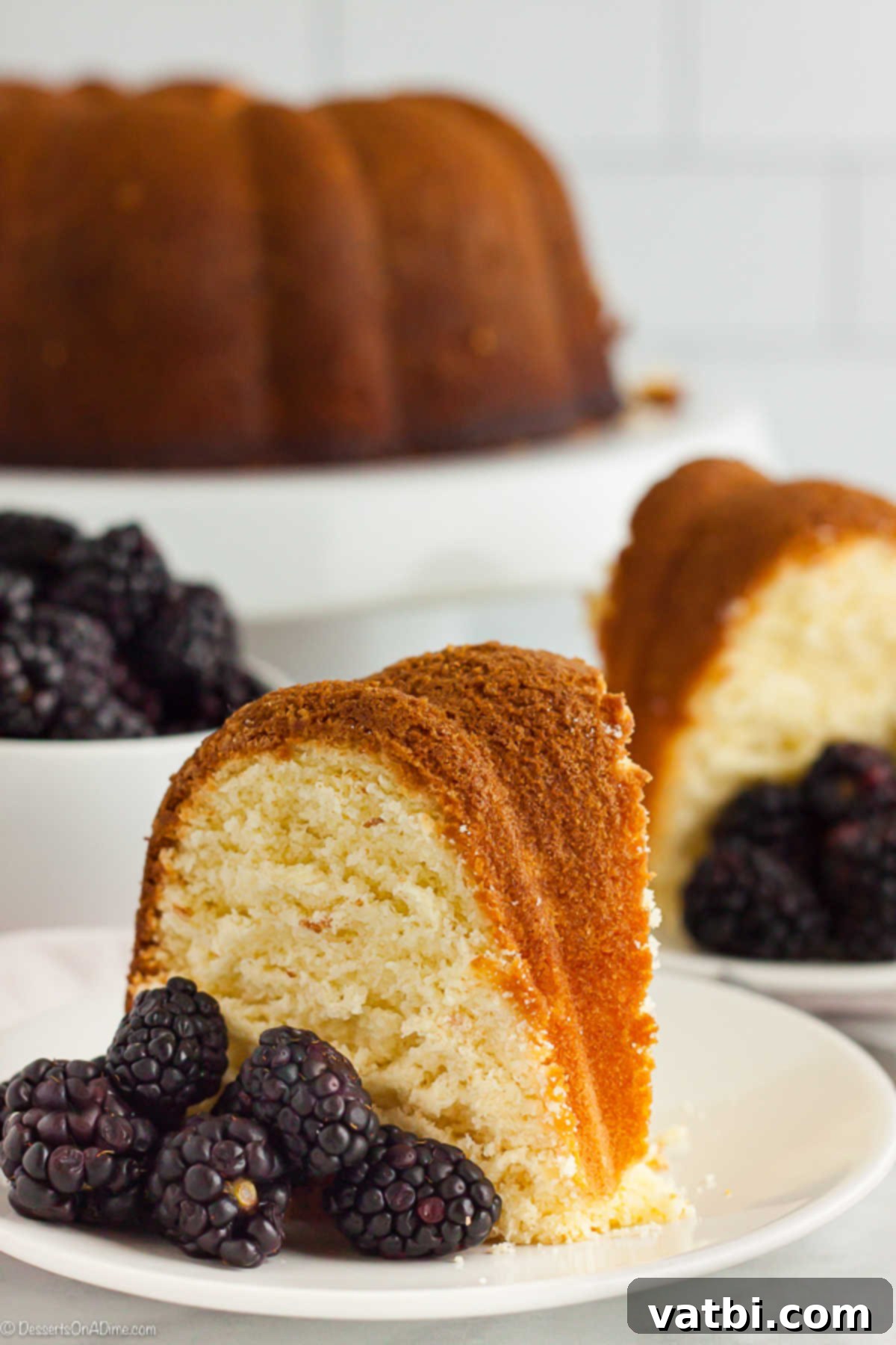 A piece of the pound cake on a white plate with blackberries on the plate.