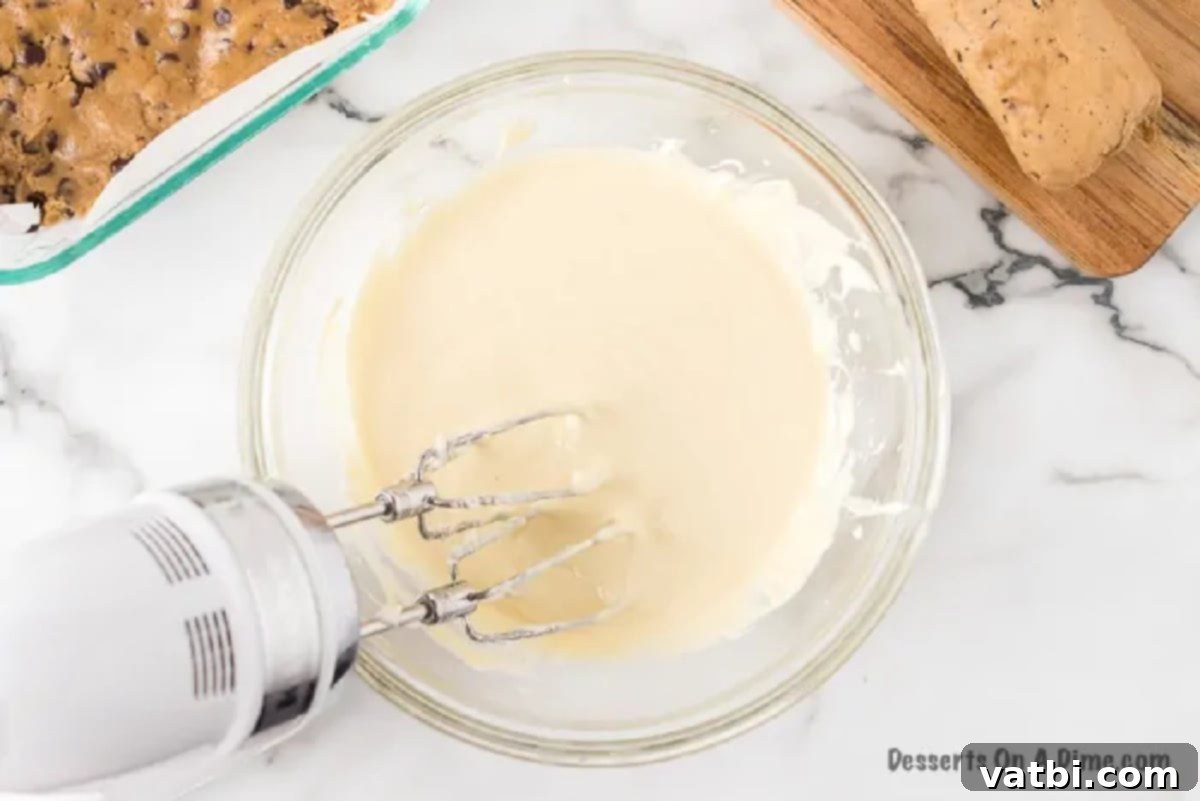 Cream cheese mixture being beaten in a bowl, appearing light and fluffy.