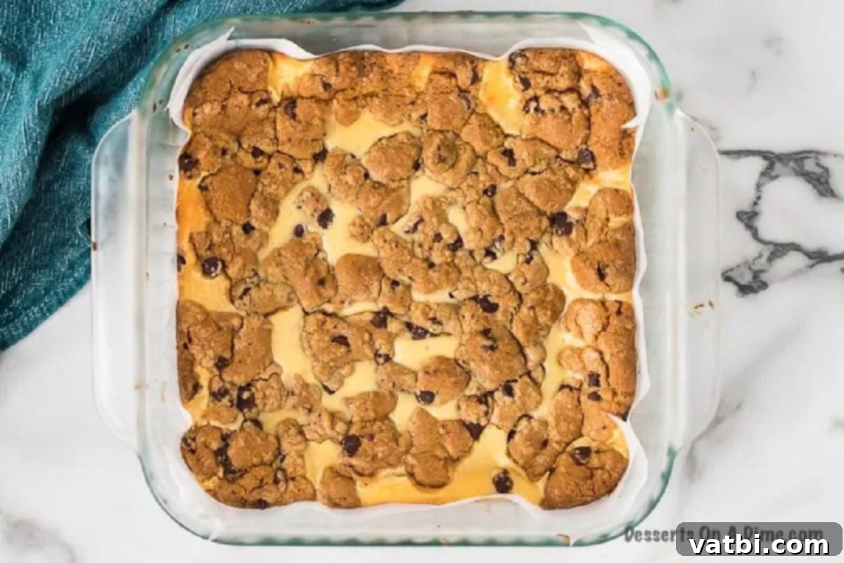 Baked chocolate chip cheesecake bars, golden brown with cookie crumble topping, still in the pan.