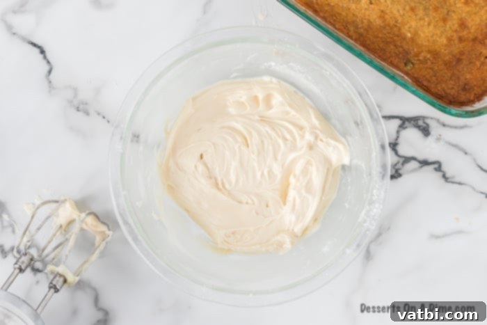 Softened cream cheese and butter are being beaten together in a bowl until smooth and fluffy.