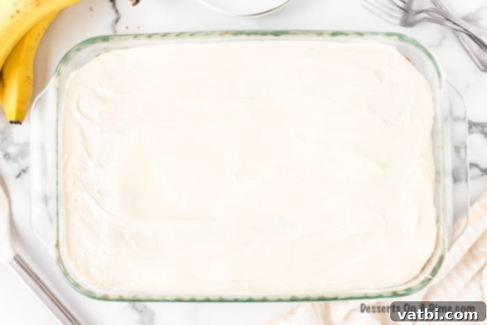 Cream cheese frosting is evenly spread over the cooled banana cake in the baking dish.