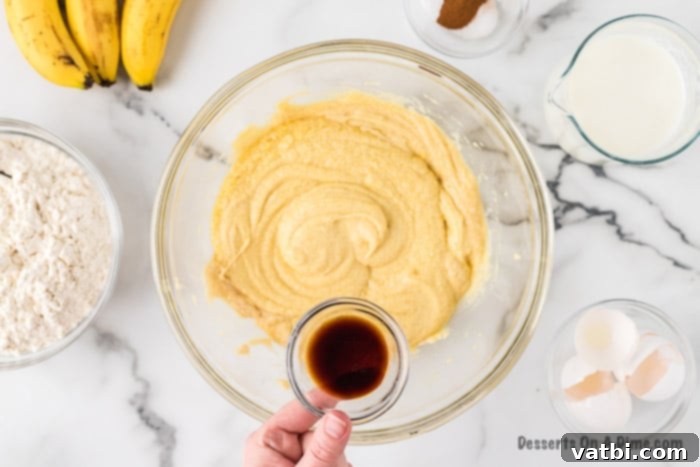 Vanilla extract is poured into the creamy mixture in a mixing bowl.