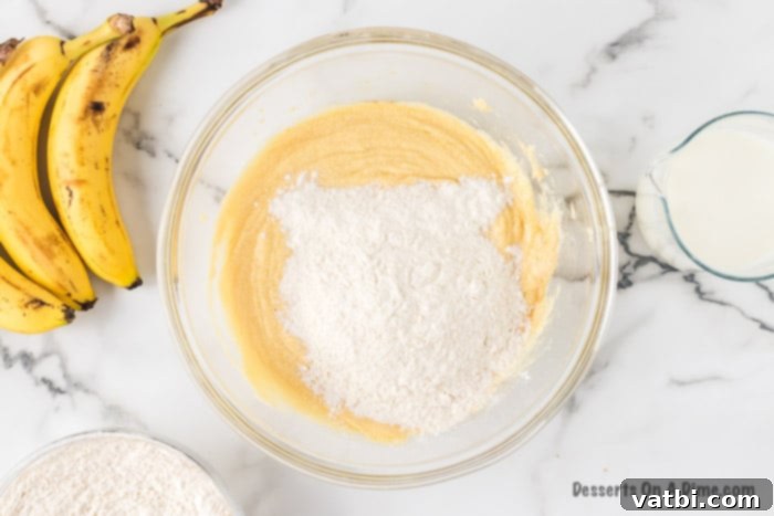 Dry ingredients, including flour, baking soda, and salt, are gradually mixed into the wet ingredients in a large bowl.