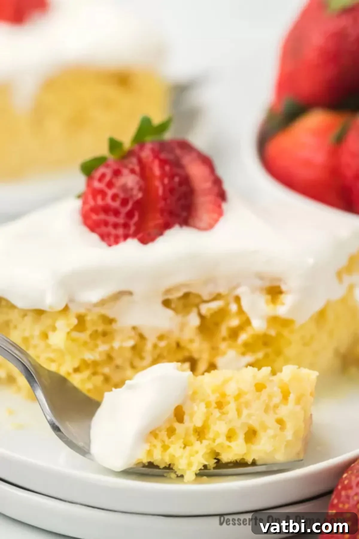A perfectly sliced piece of Tres Leches Cake on a white plate, showcasing its moist texture and creamy whipped topping.