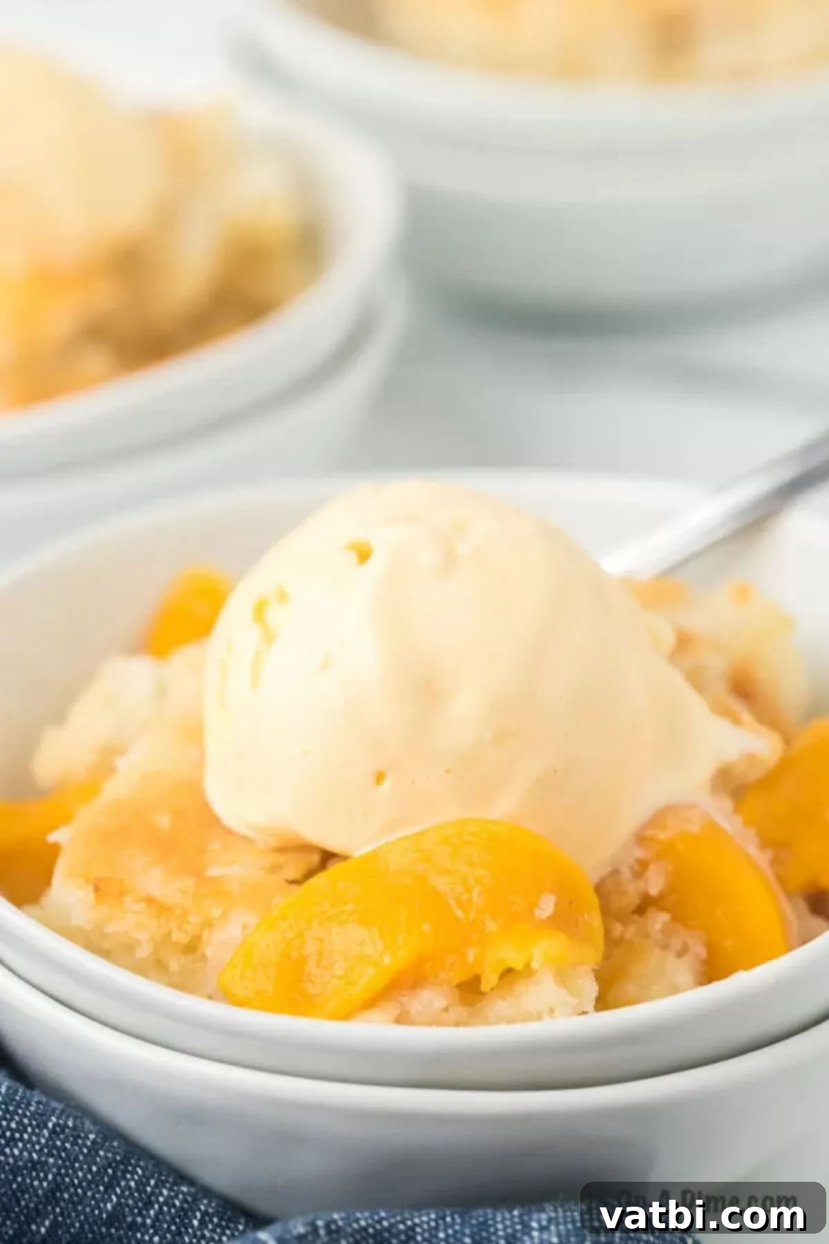 This old fashioned peach cobbler is the best recipe and you likely already have all the ingredients to make this today. Just add ice cream. Peach Cobbler in a bowl topped with ice cream, showcasing its golden crust and juicy fruit.
