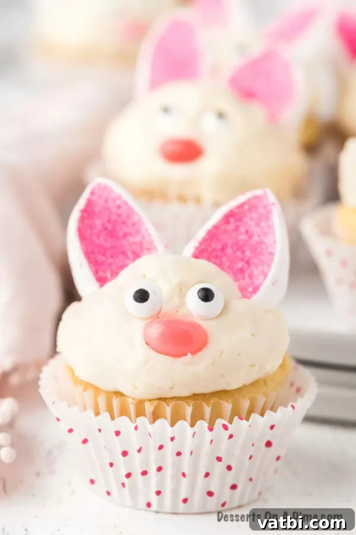 Two decorated Easter Bunny Cupcakes ready to be enjoyed, showcasing their cute marshmallow ears, candy eyes, and jelly bean noses against a blurred background.