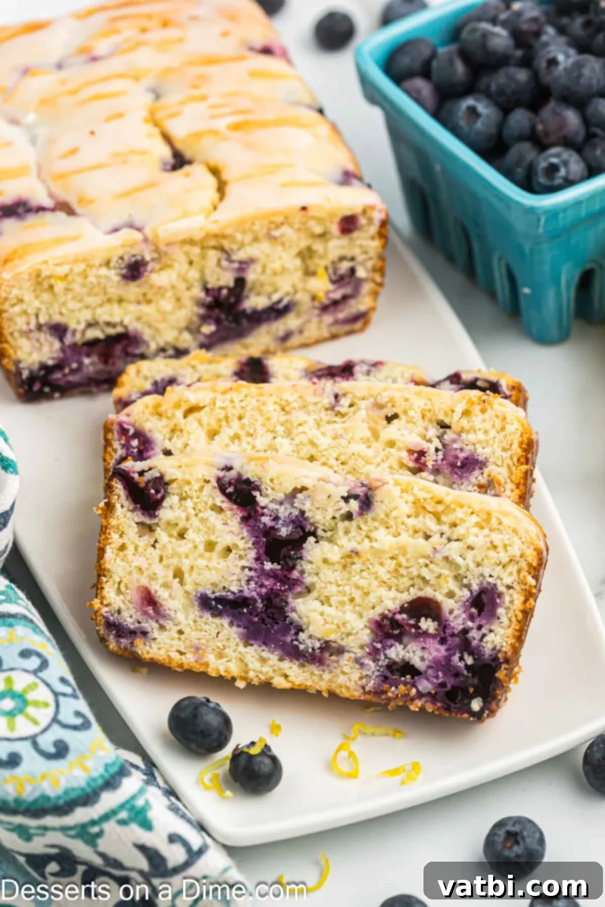 Zesty Lemon Blueberry Loaf 2 Slices of moist Lemon Blueberry Bread on a white plate, garnished with fresh blueberries and lemon zest.