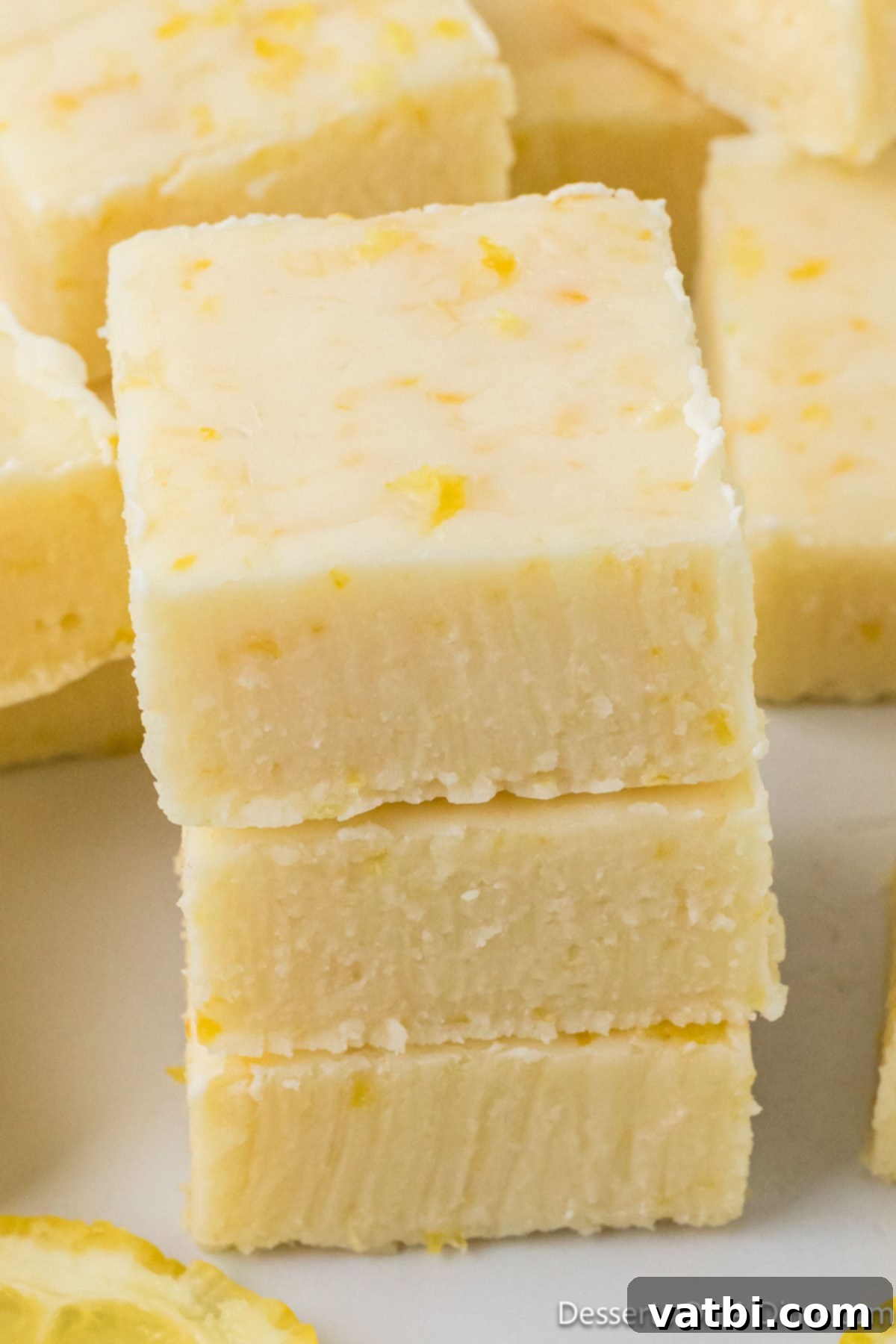 Lemon fudge squares stacked neatly on a white background, showcasing their creamy texture and vibrant color. 
