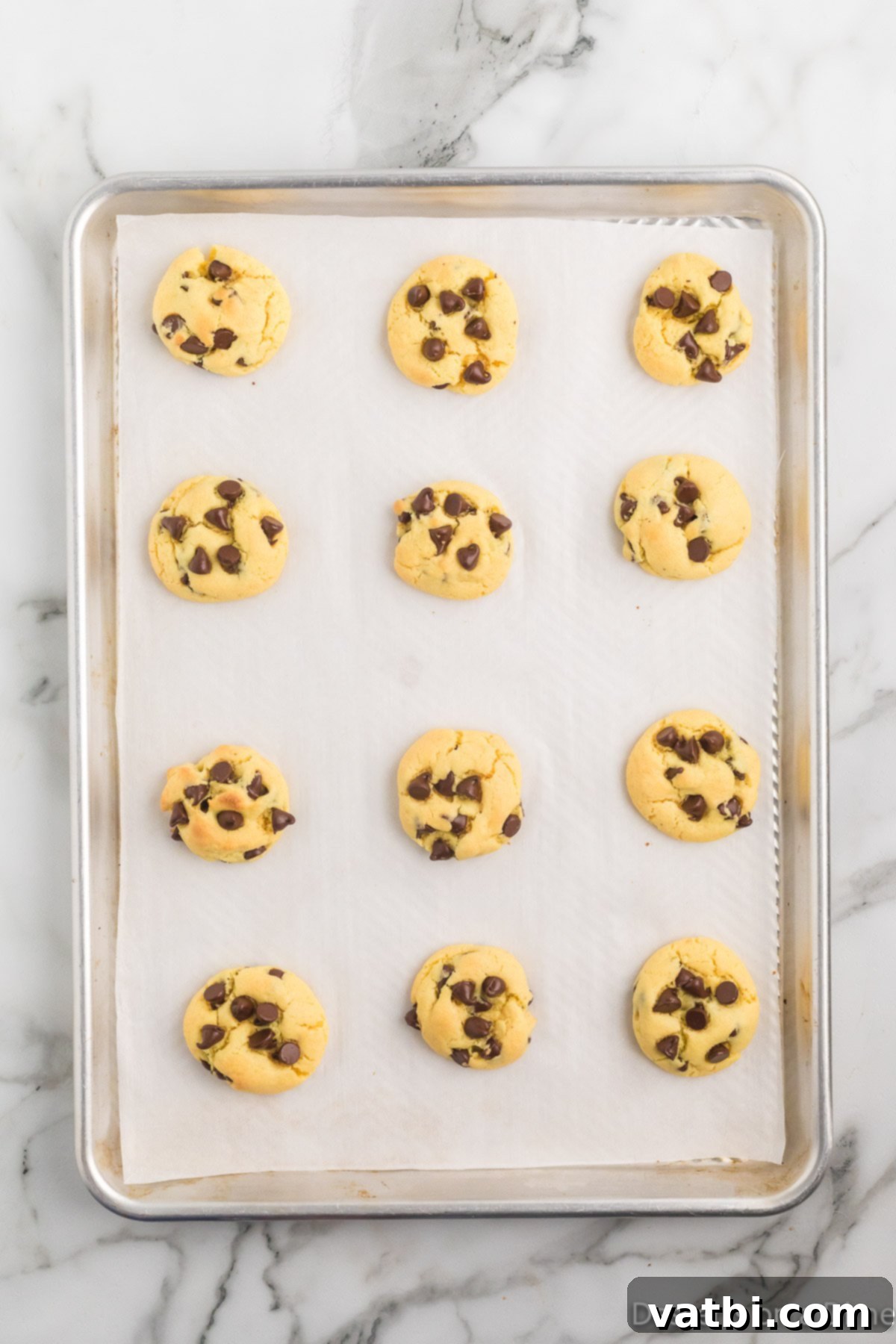 Perfect Chocolate Chip Cake Mix Cookies 7 Freshly baked Chocolate Chip Cake Mix Cookies cooling on a baking sheet, showing their slightly golden edges and soft, inviting centers.
