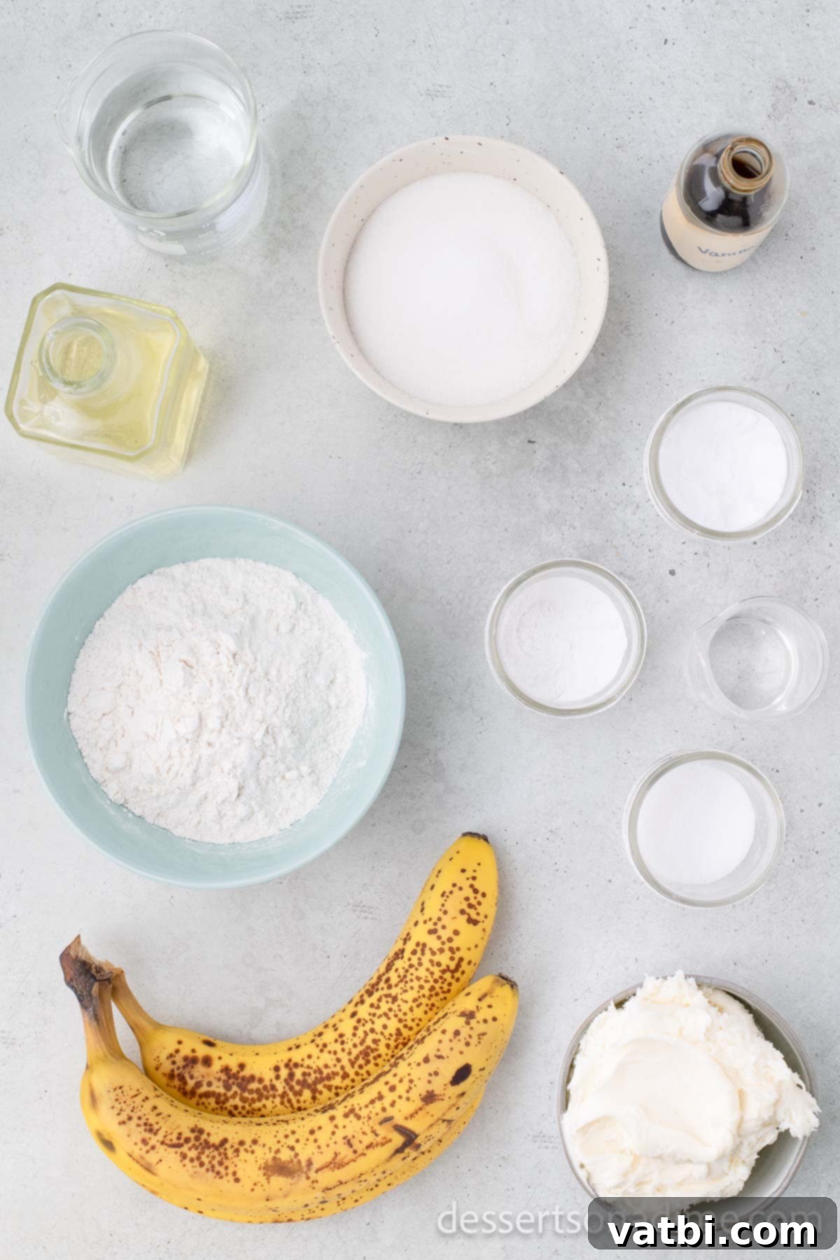 Wildly Delicious Banana Cake 3 A flat lay photograph displaying the simple ingredients required for Crazy Banana Cake: all-purpose flour, granulated sugar, baking soda, baking powder, salt, vanilla extract, white vinegar, vegetable oil, water, and perfectly overripe bananas.