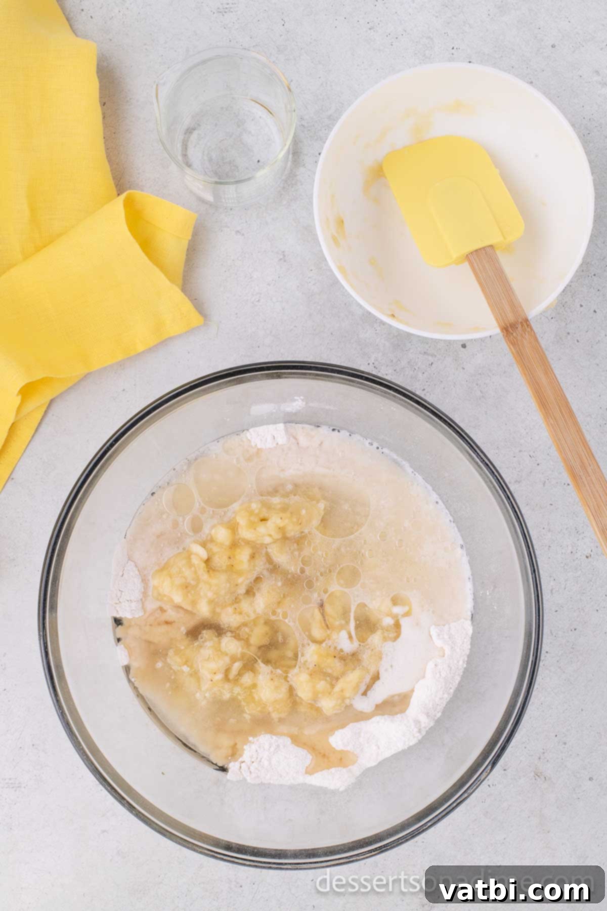 Wildly Delicious Banana Cake 7 Mashed overripe bananas and water added directly on top of the dry ingredients and other wet components in the mixing bowl, ready for combining.