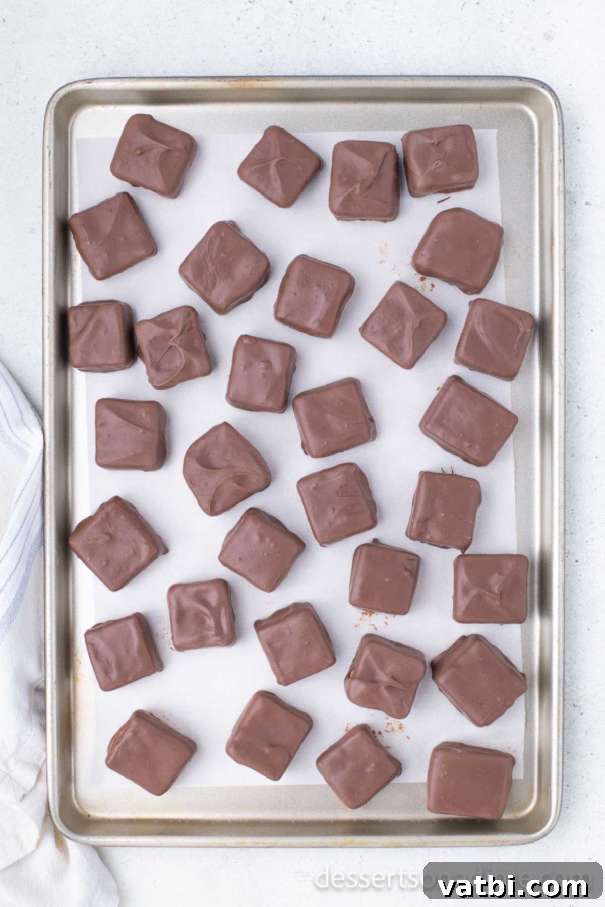 Chocolate-dipped candy squares placed back on the baking sheet to set in the freezer.