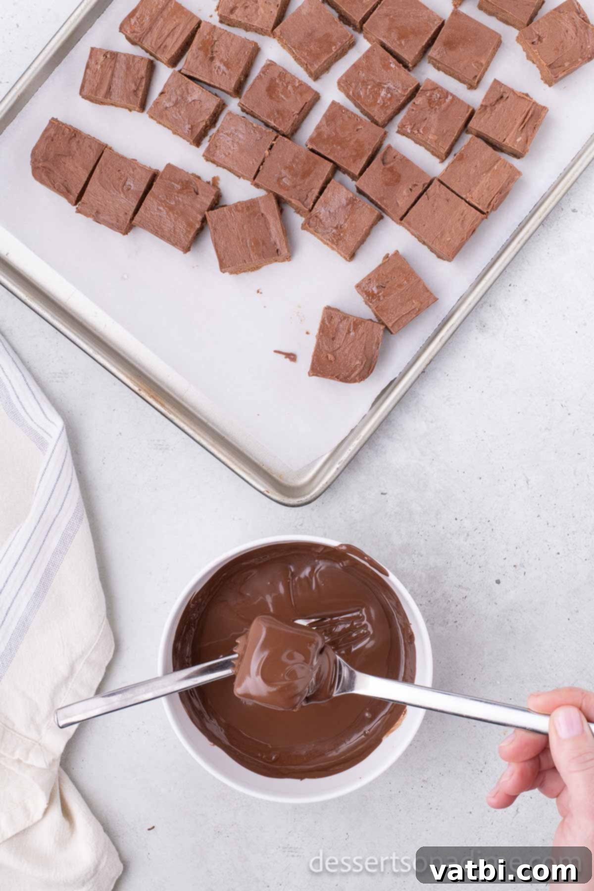Individual candy squares being dipped into melted chocolate wafers using forks.