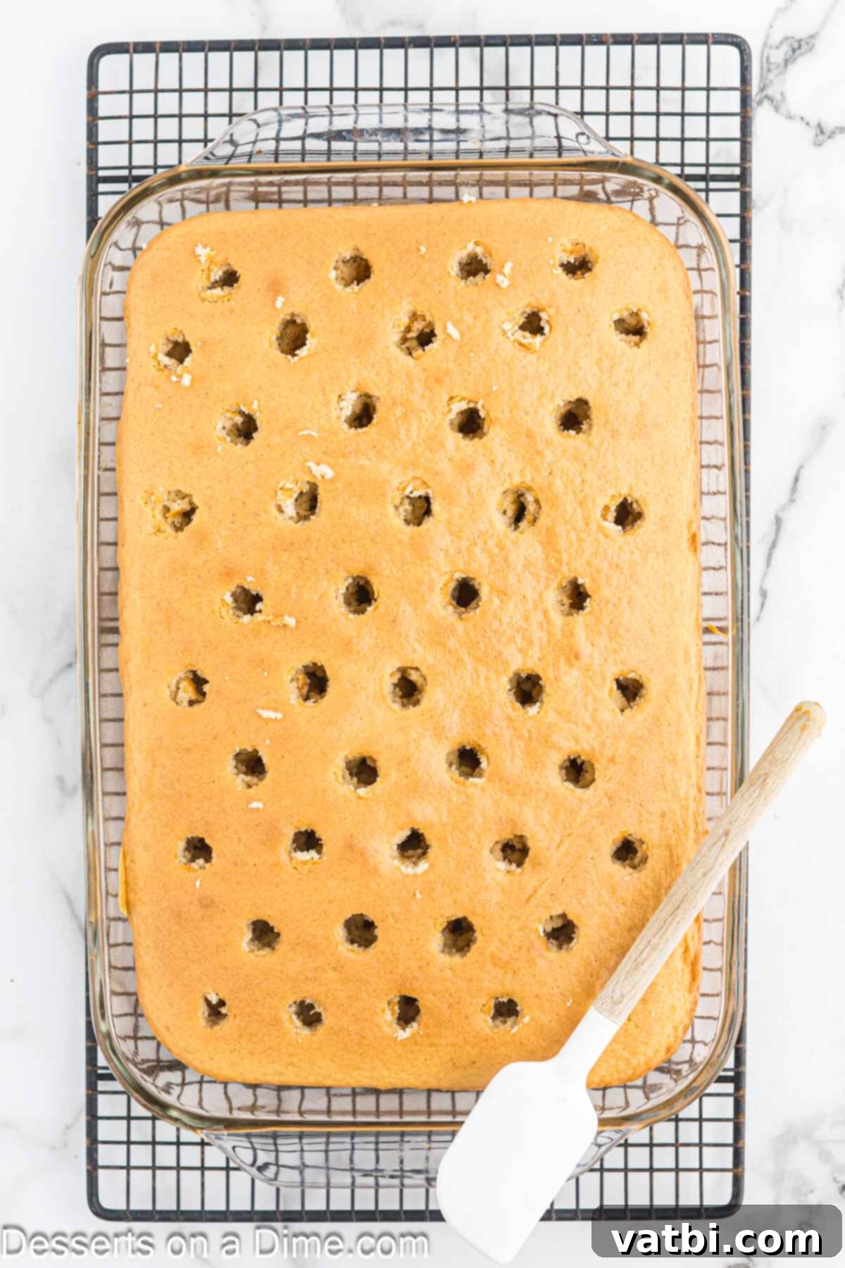 Cinnamon Whiskey Poke Cake 5 Baked cake with holes poked across its surface using a wooden spoon handle.