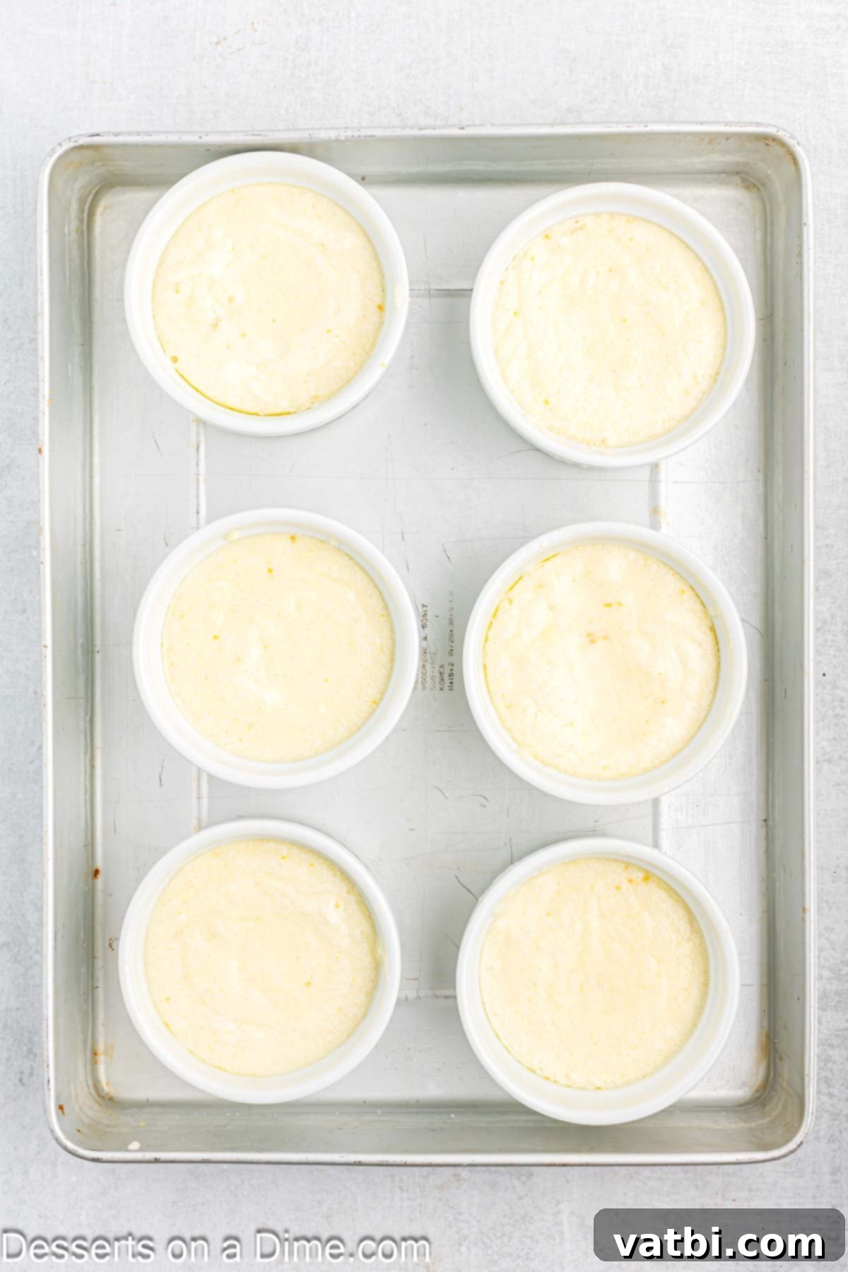 Zesty Lemon Pudding Cake 8 Batter being poured evenly into prepared ramekins placed in a large baking pan.