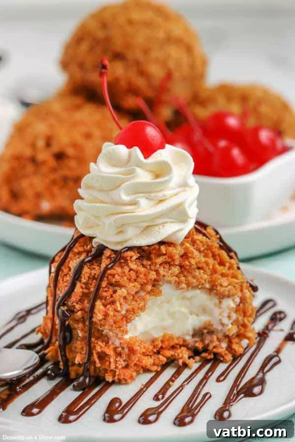 Enjoy deep fried ice cream recipe at home with this recipe. The crispy outside and the creamy ice cream combine for a restaurant style treat. Deep Fried Ice Cream on a white plate topped with whipped cream and cherries