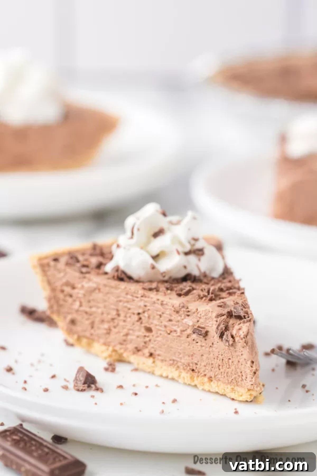 A delectable slice of No Bake Hershey Pie resting on a white plate, topped with whipped cream and chocolate shavings.