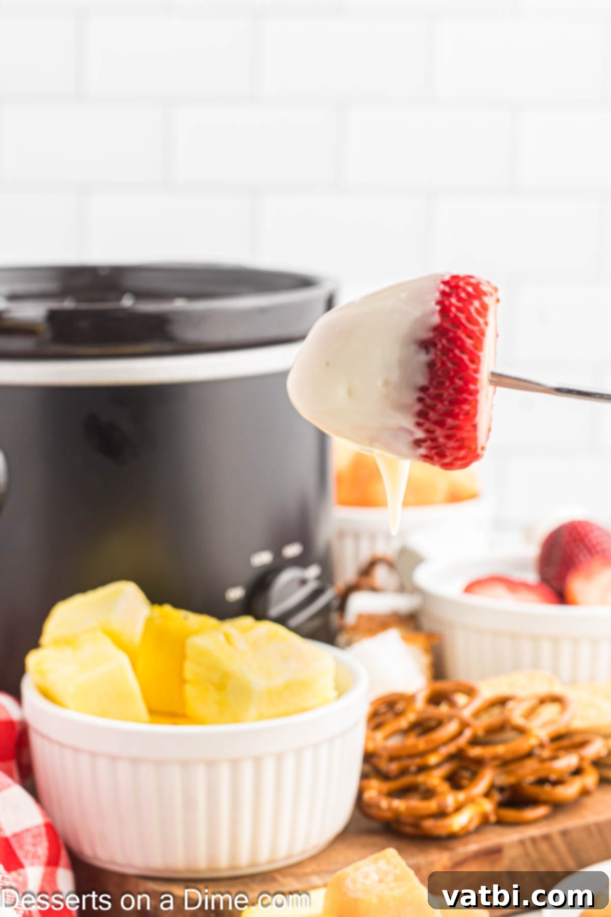 Decadent White Chocolate Fondue 2 Fondue with fresh fruit being served from a white ceramic fondue pot.