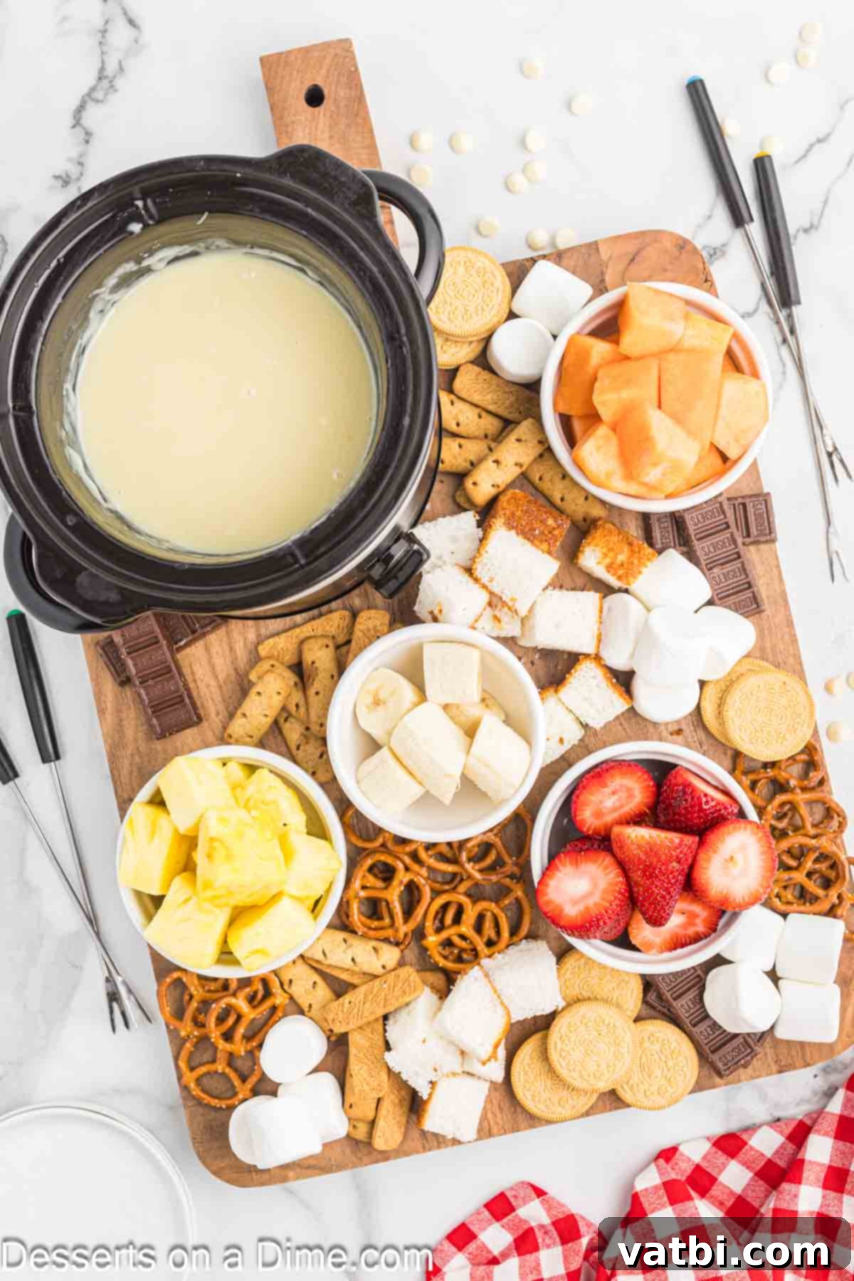 Decadent White Chocolate Fondue 5 Melted white chocolate fondue in a crock pot, surrounded by various dippers on a platter.