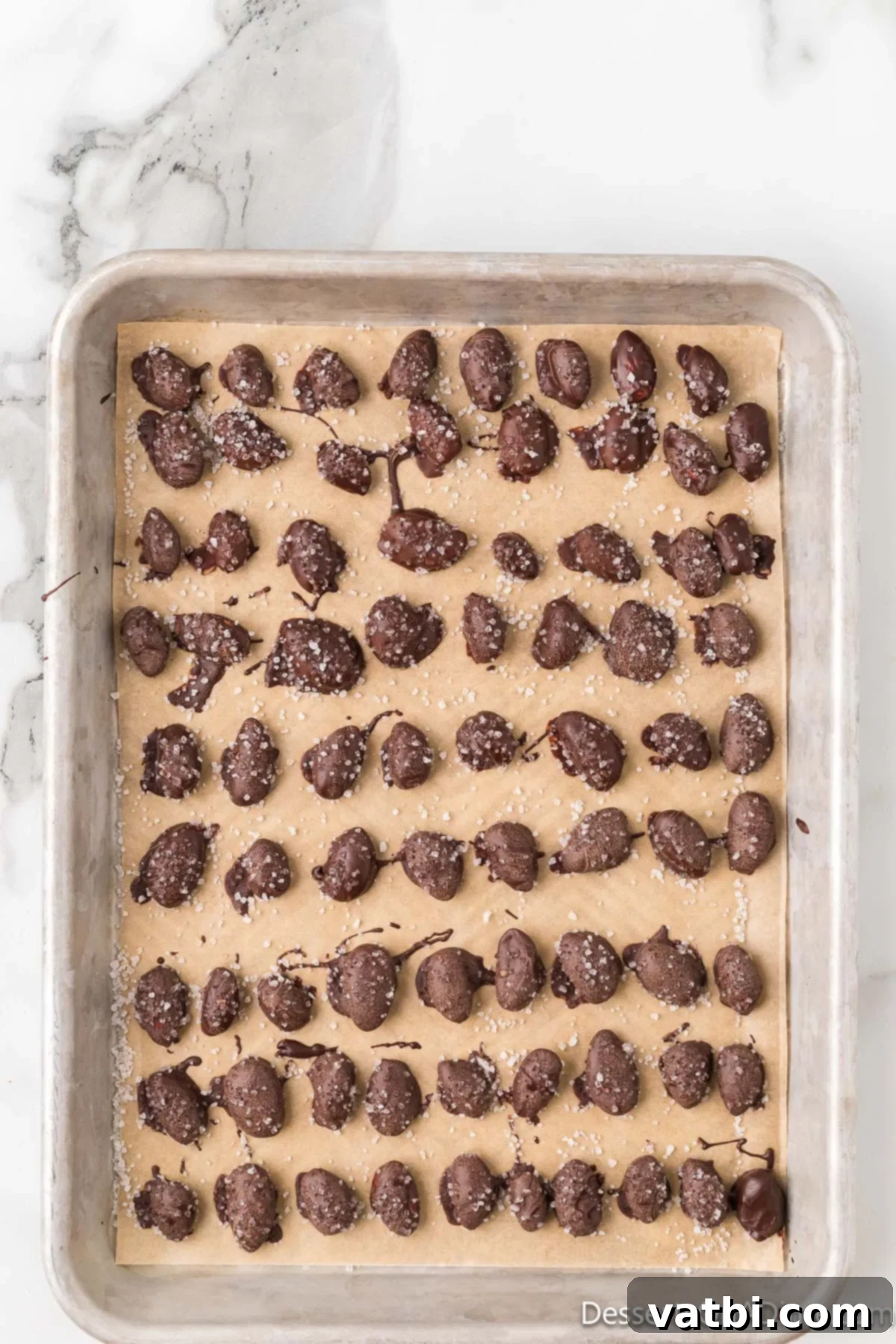 Midnight Almond Delights 9 Almonds coated in chocolate and topped with sea salt on baking sheet.