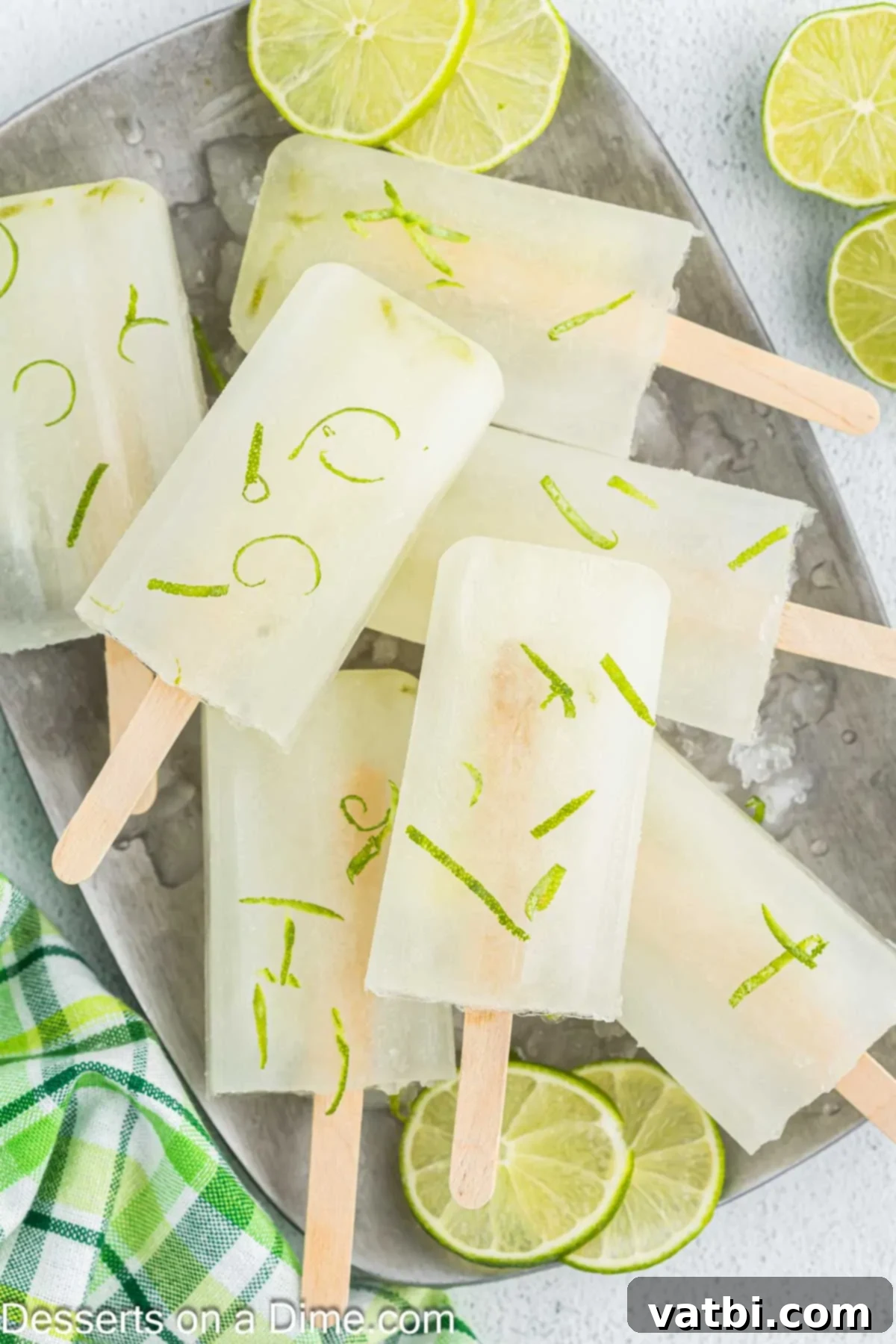 Enjoy light and refreshing lime popsicles when you make this recipe. It is the perfect summer time treat and the entire family will enjoy. A close-up of vibrant green homemade lime popsicles with visible lime zest, set against a summer backdrop, suggesting a refreshing treat.