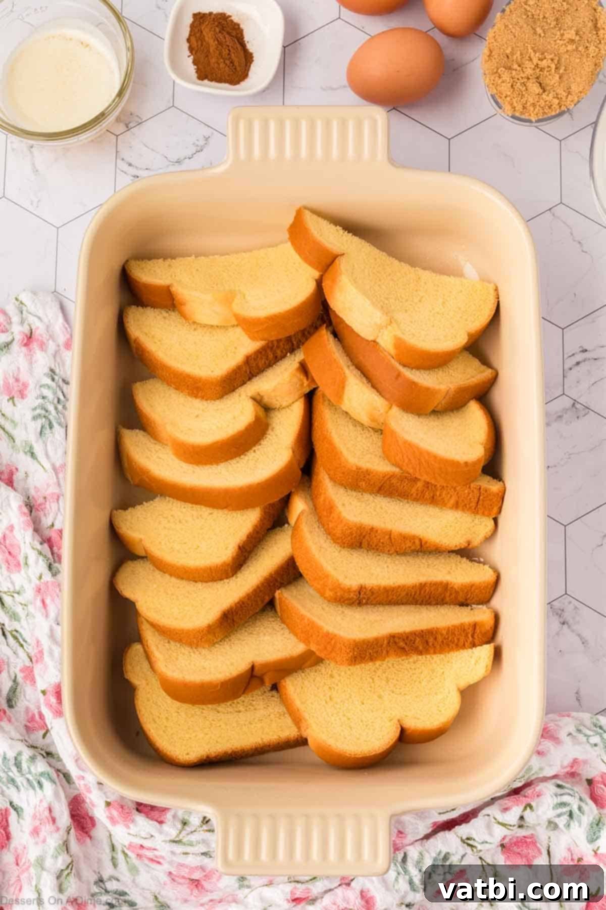 Neatly layered slices of brioche bread in a baking dish, forming the base of the bread pudding.