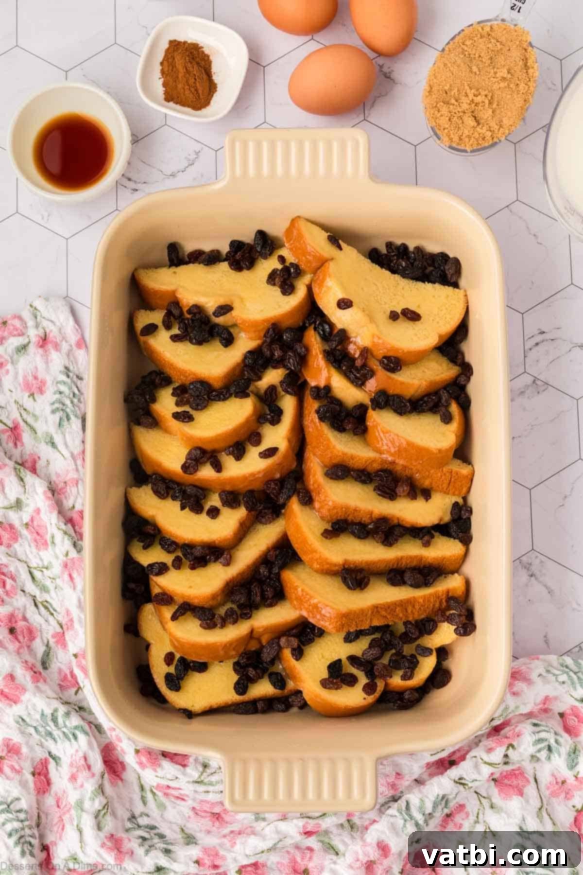 Golden raisins sprinkled generously over buttered bread slices in a baking dish.