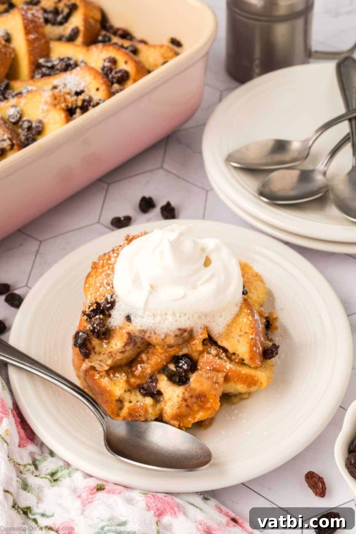 A serving of warm bread and butter pudding on a white plate, garnished with a dollop of whipped cream and a mint sprig.