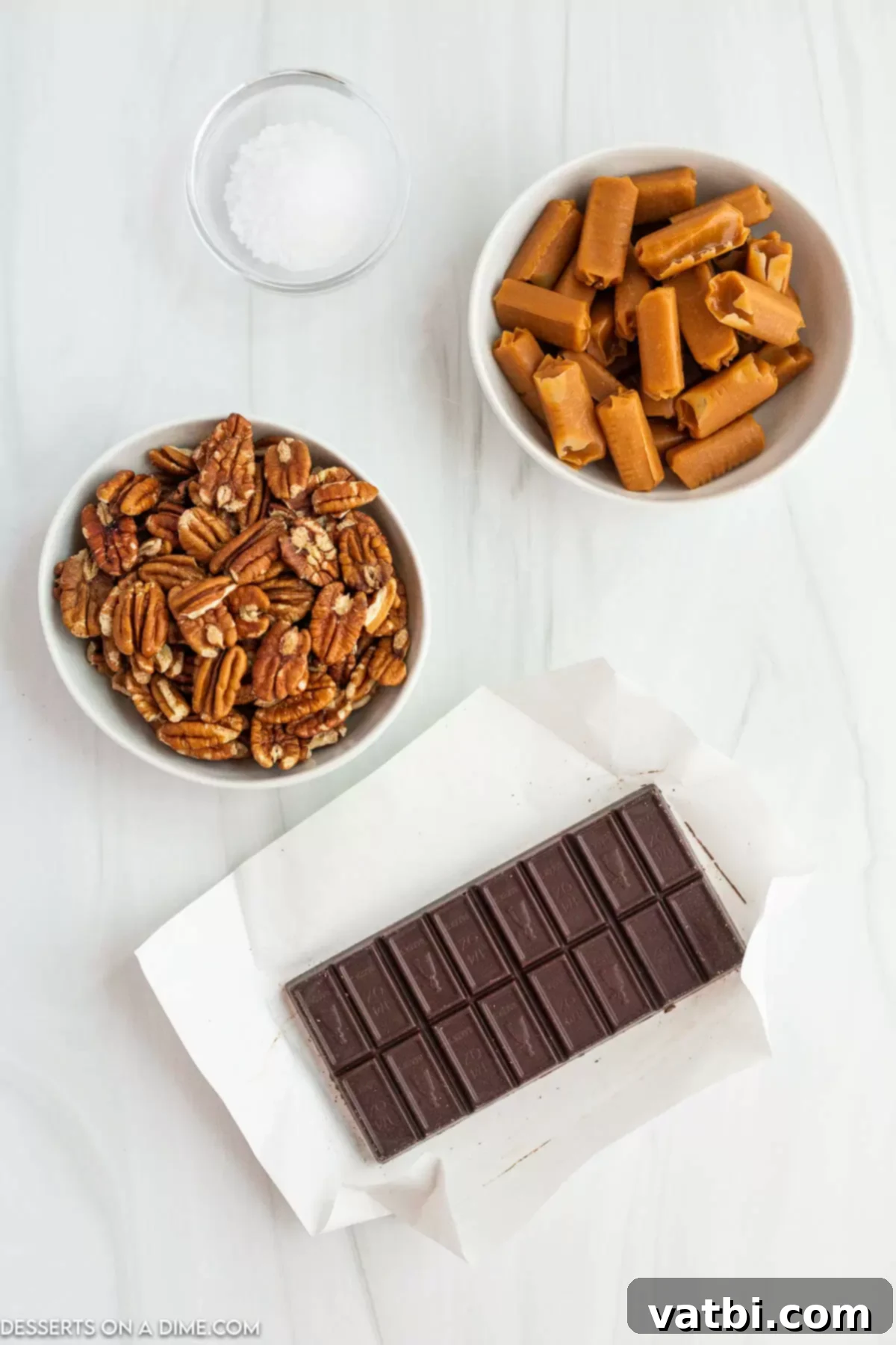 Ingredients laid out for making chocolate turtles: pecan halves, individually wrapped caramels, heavy whipping cream, semi-sweet melting chocolate chips, and a small pile of sea salt.
