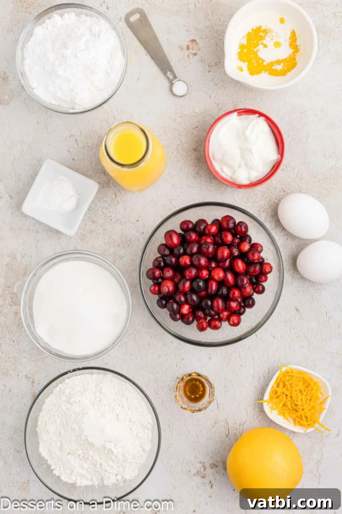 Zesty Orange Cranberry Loaf 3 A selection of fresh ingredients laid out on a table for making orange cranberry bread, including Greek yogurt, melted butter, orange juice, orange zest, eggs, granulated sugar, flour, baking powder, and fresh cranberries.