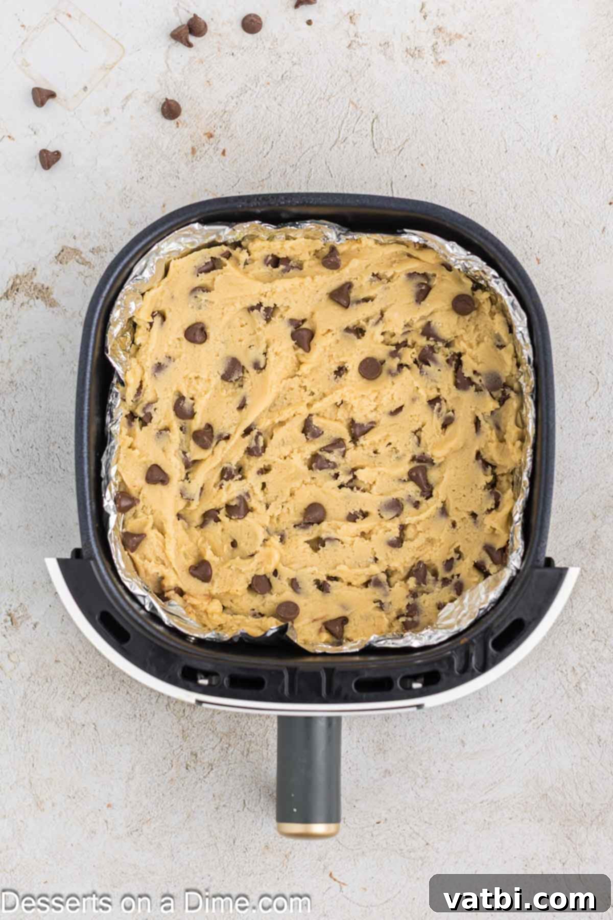 Chocolate chip cookie dough pressed evenly into the foil-lined air fryer basket.
