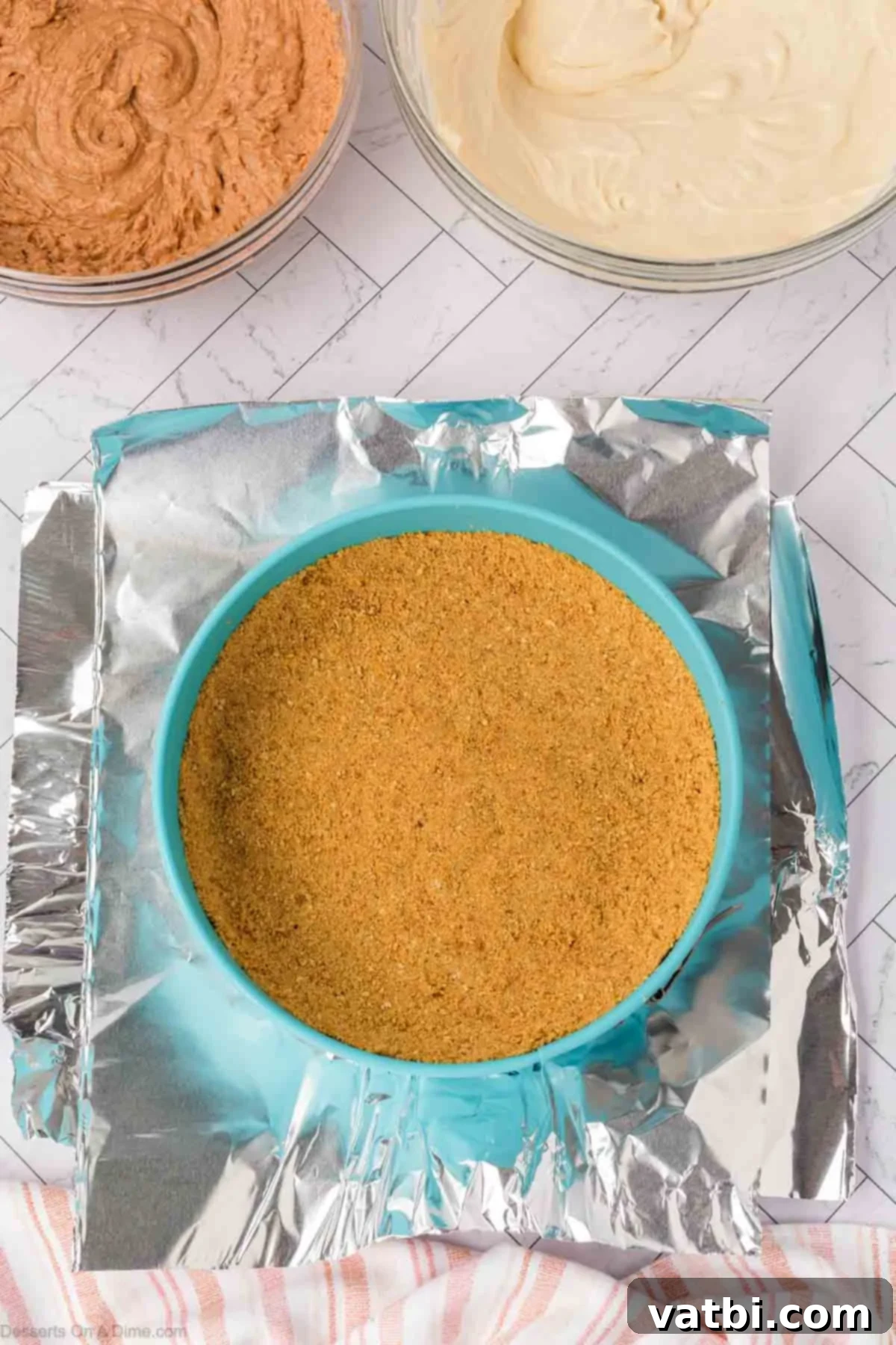 A springform pan wrapped in aluminum foil, placed inside a larger roasting pan for a water bath setup.