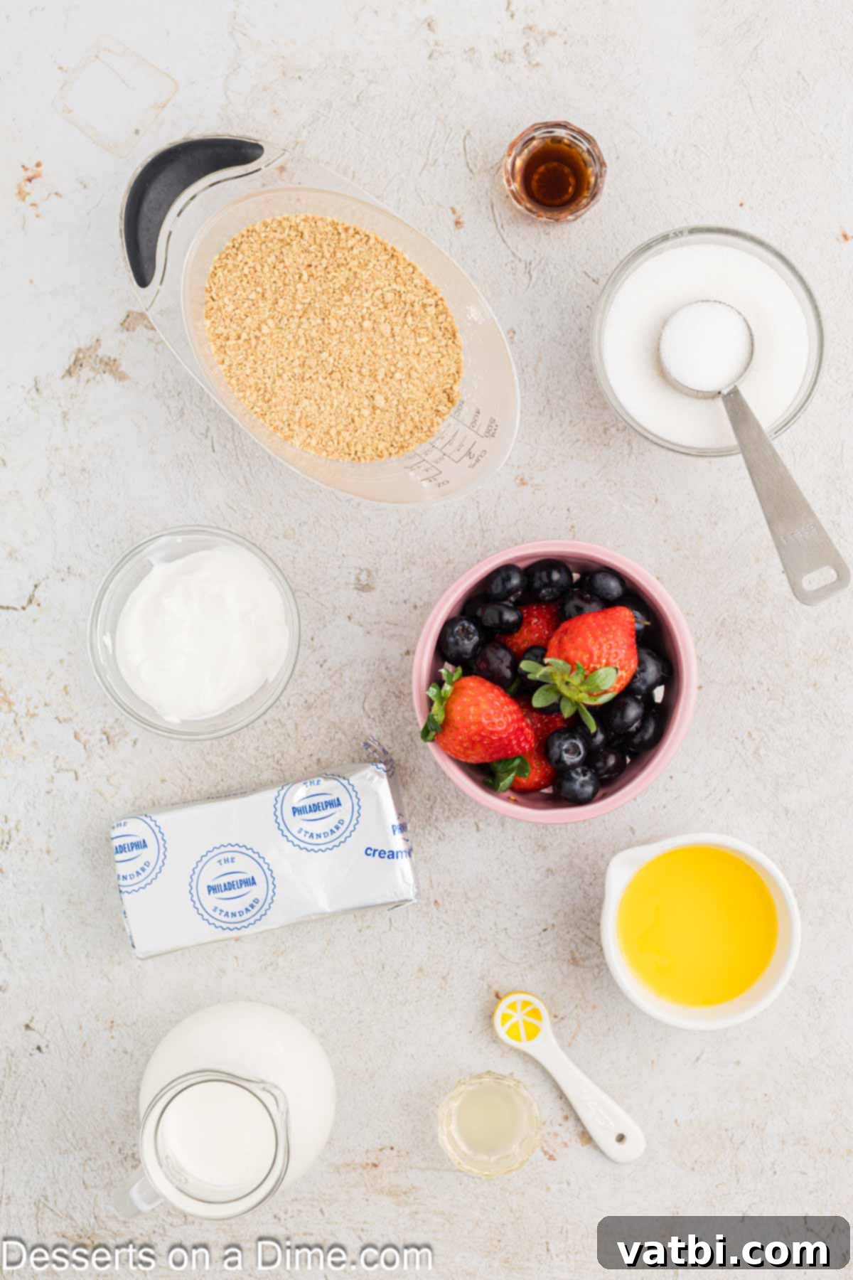 A beautiful display of ingredients needed to make mini cheesecake bites, including graham crackers, sugar, butter, heavy cream, cream cheese, sour cream, lemon, vanilla, and fresh berries.