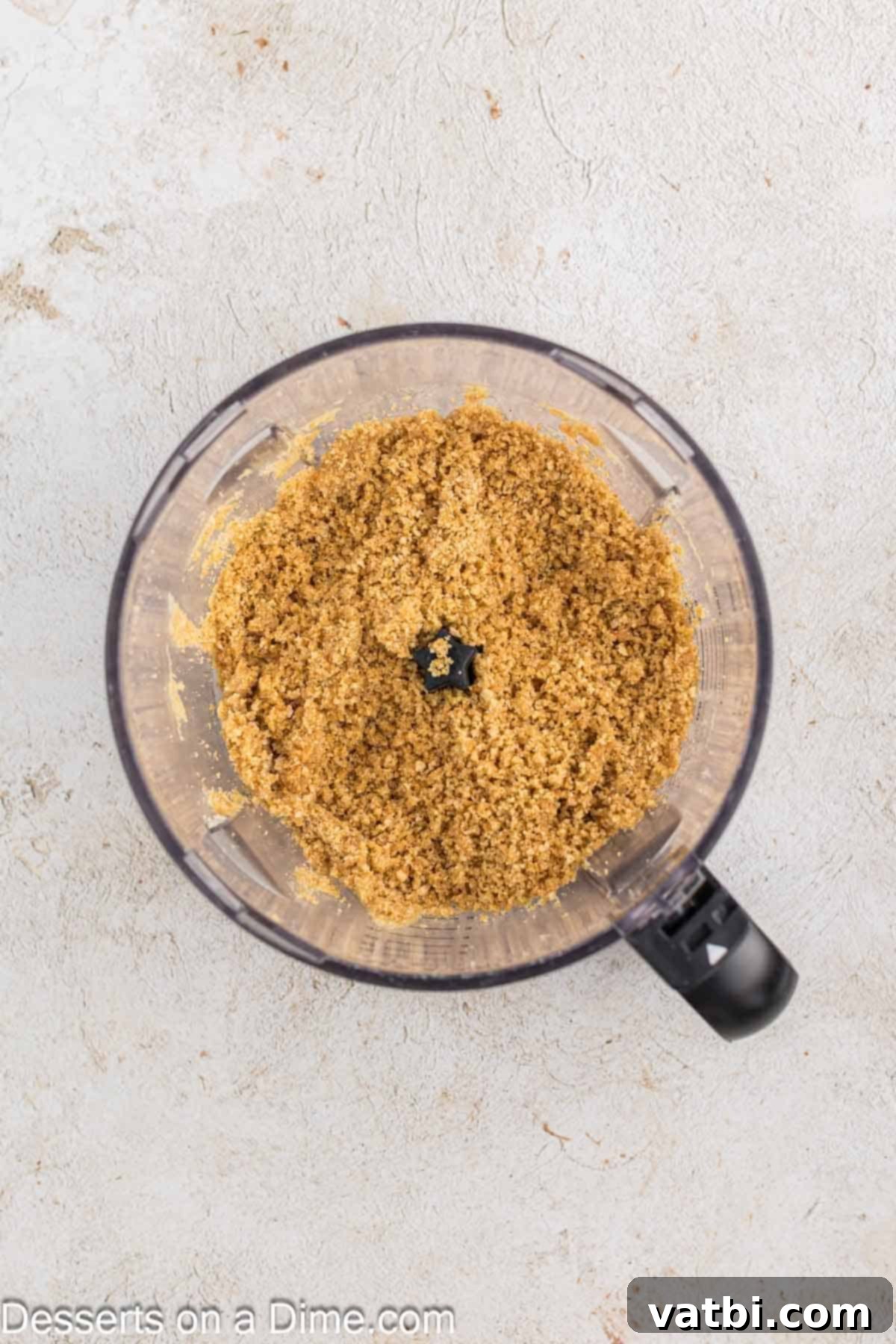 Graham cracker crumbs being pulsed in a food processor until finely ground, ready to form the base of the mini cheesecakes.