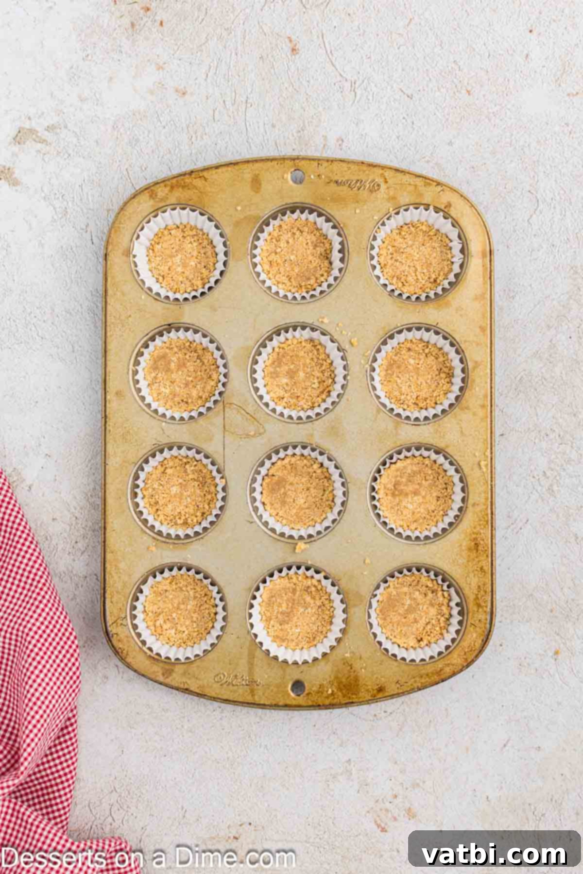 Graham cracker crumbs neatly pressed into the bottom of mini muffin liners, creating a solid crust base for the cheesecake filling.
