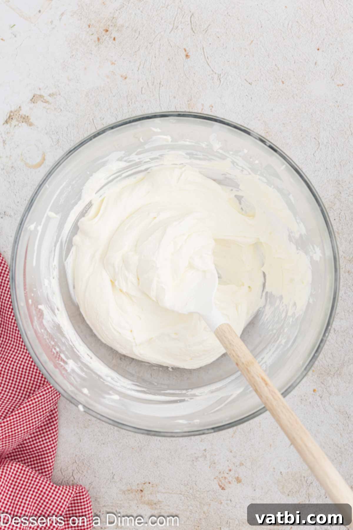 Whipped cream being gently folded into the cream cheese mixture using a rubber spatula to maintain its airy texture.