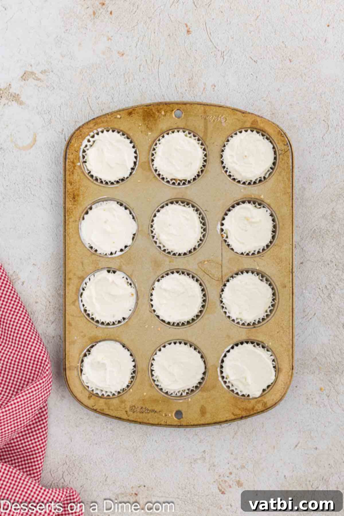 Cream cheese mixture being carefully added into each muffin liner on top of the prepared crust, filling them about ¾ full.